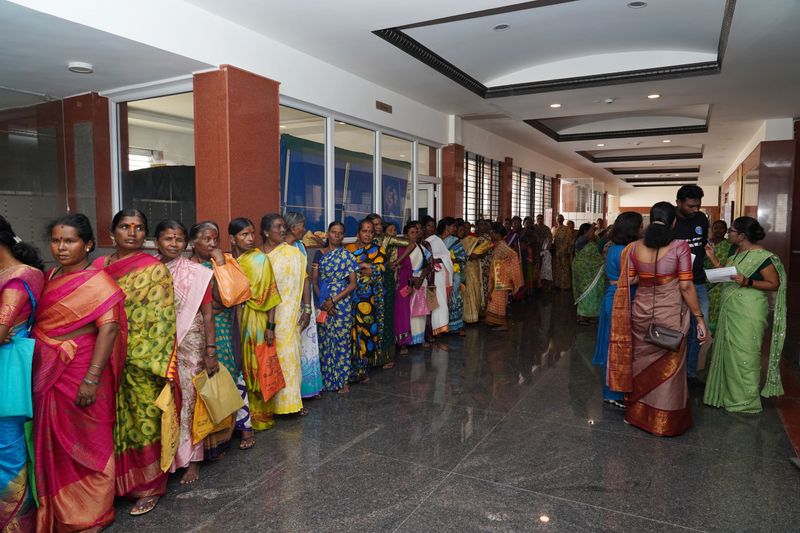A long queue of women wait in an indoor hallway to register for a community health camp.