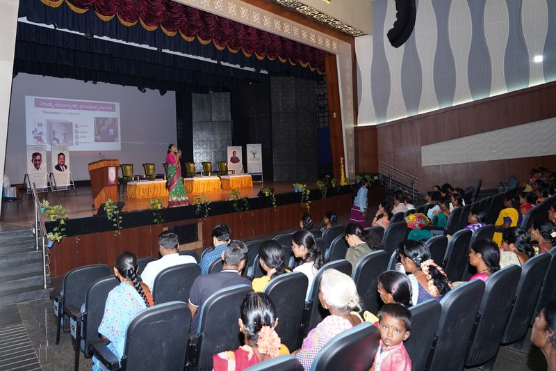 An audience of women and a child watch a presentation on a screen during a community talk.