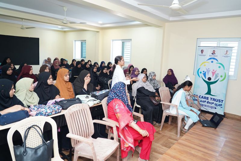 A health worker addresses a seated group of women, several wearing hijabs, during a health education class.