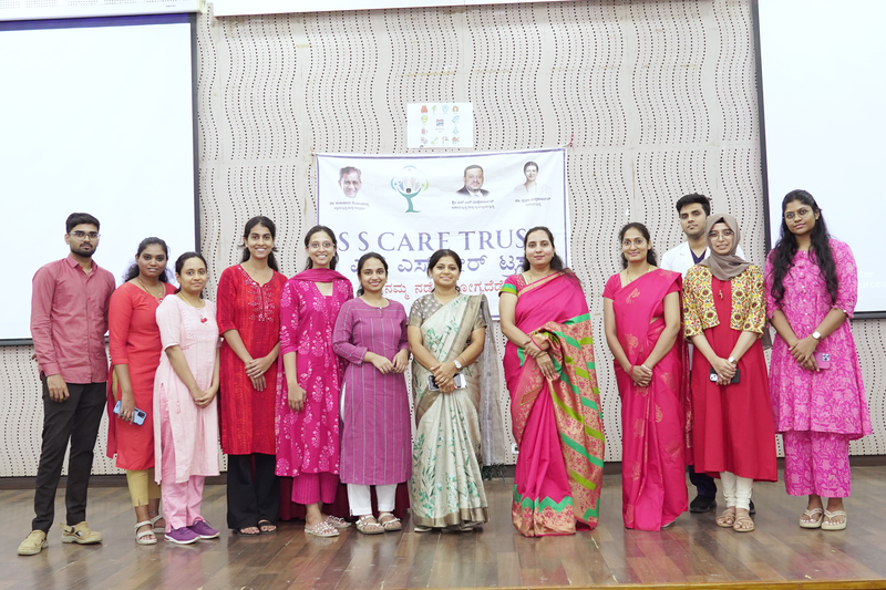 A group of staff and volunteers pose together on stage in front of an SS Care Trust banner.