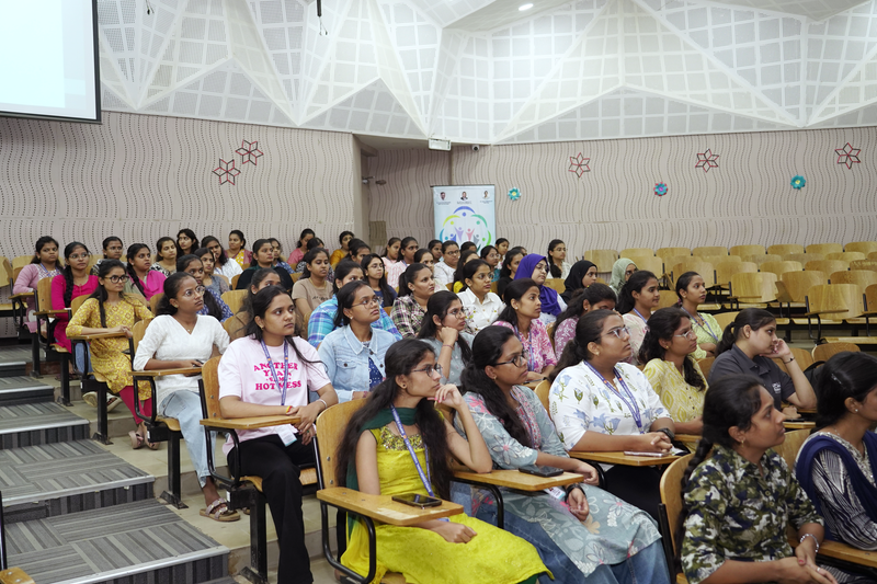 Young women sit in rows in an auditorium, attending a health awareness talk.