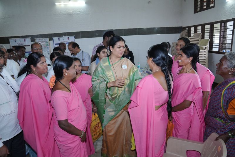 Community health workers in pink sarees gather around a staff member during a women's outreach visit.