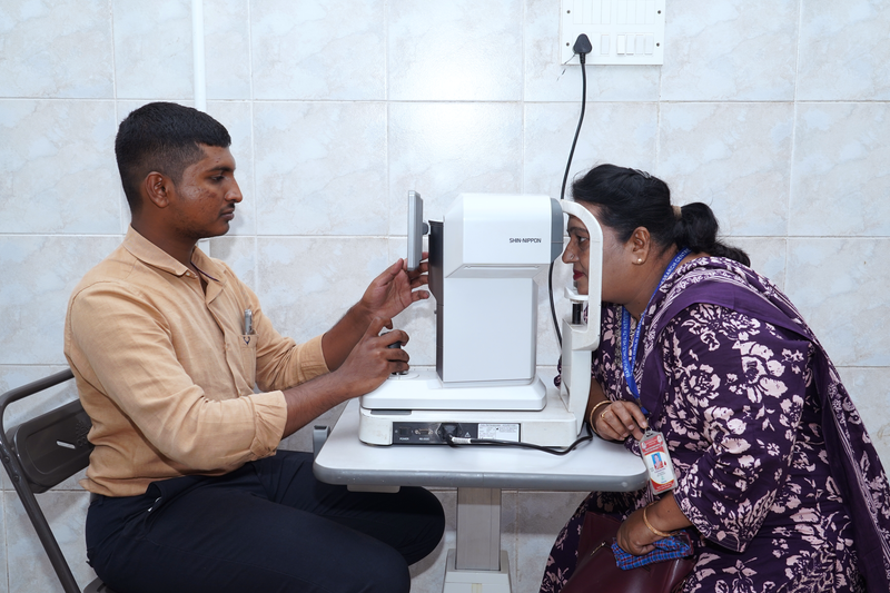 An optometrist examines a woman's eyes using diagnostic equipment at a community health camp.