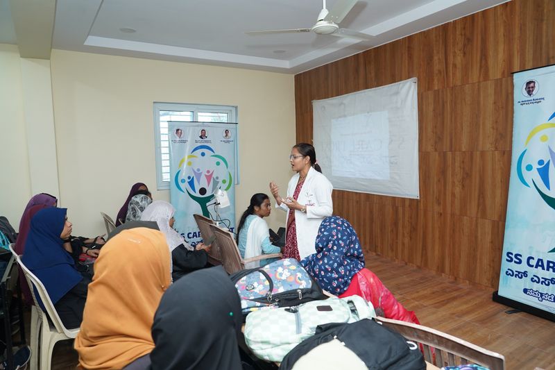 A health educator in a white coat addresses a group of young women during an outreach health talk.