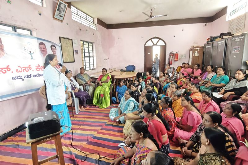 A health educator speaks to women gathered on a colourful carpet during a community health talk.