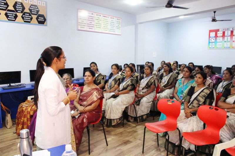 A health worker addresses a group of women seated in a classroom during a health education session.