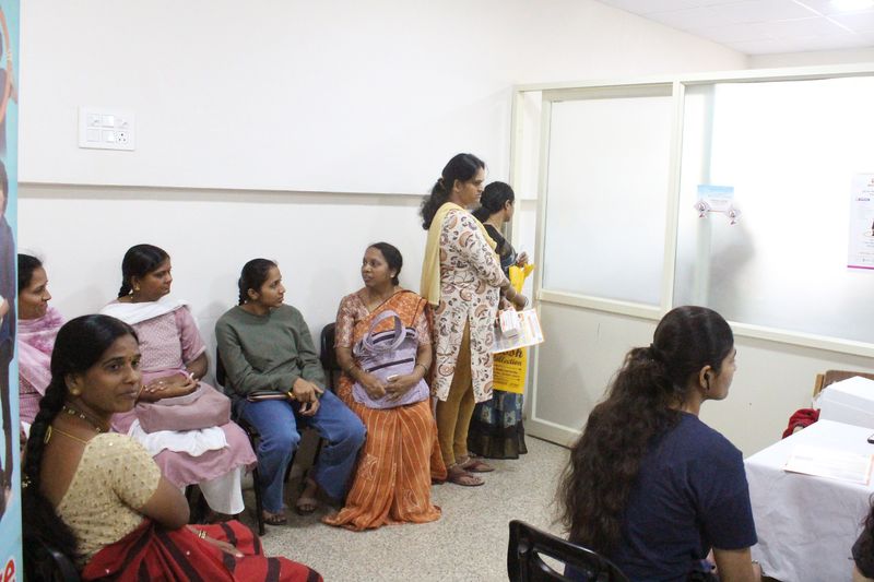 Women sit and stand in a waiting area outside a clinic room during a women's health screening camp.