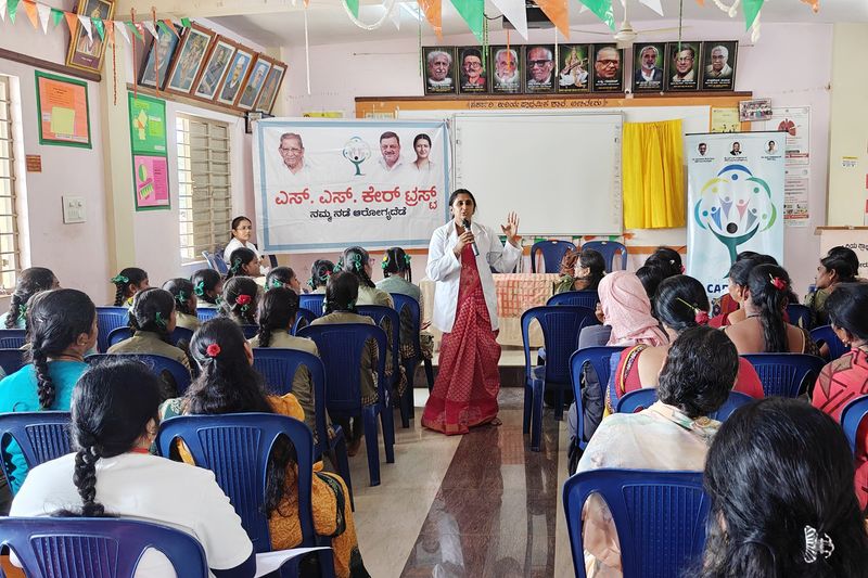 A health worker speaks on a microphone to a hall of schoolgirls during an adolescent health awareness session.
