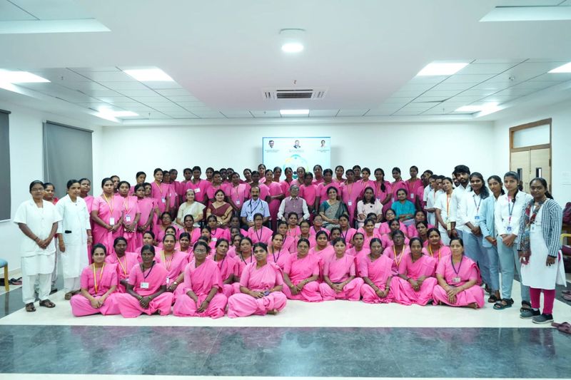 Dozens of women in pink sarees sit and stand for a group photo in a decorated hall after a training session.