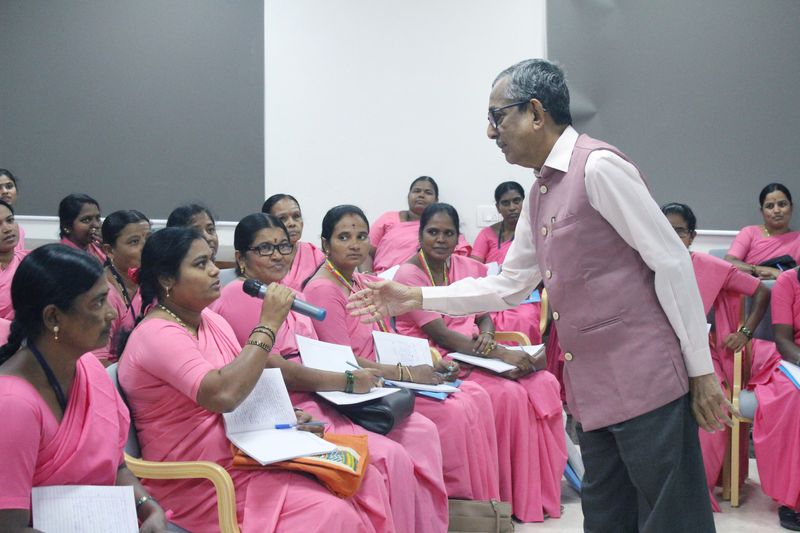 A facilitator leans in to hand a microphone to a seated woman asking a question during a group health talk.