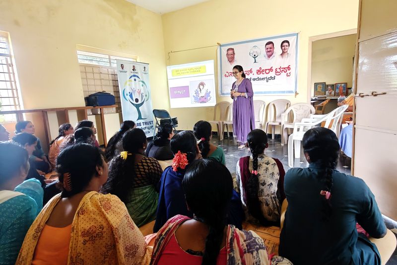 A facilitator speaks to young women and girls seated on the floor during a health awareness talk.