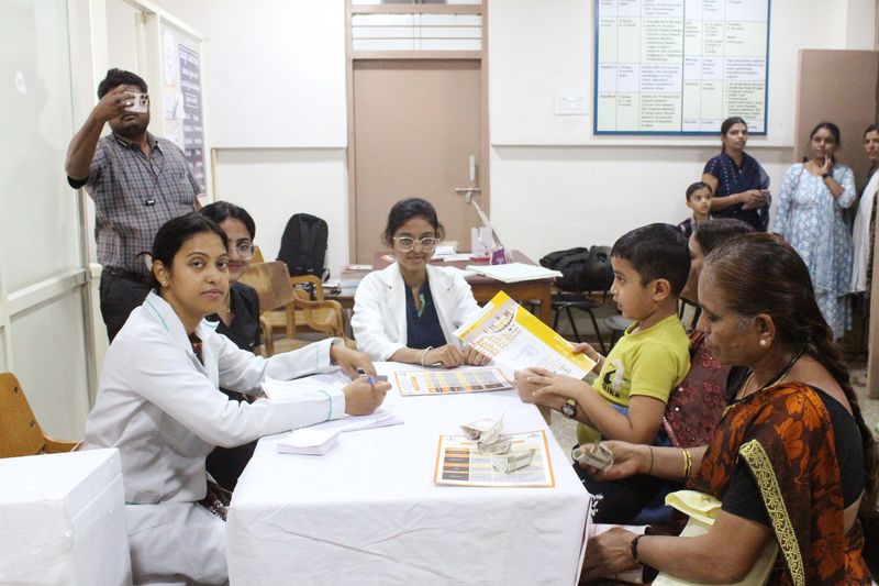 Staff fill out forms at a table while a boy and an elderly woman look on during a family health camp.