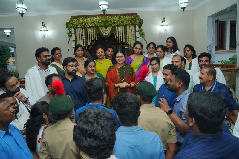 Volunteers and staff, including two in scout uniforms with red-plumed berets, gather indoors near a decorated doorway.