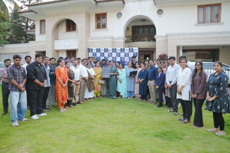 A group of volunteers and staff stand together on a lawn in front of a large house, one holding a certificate.