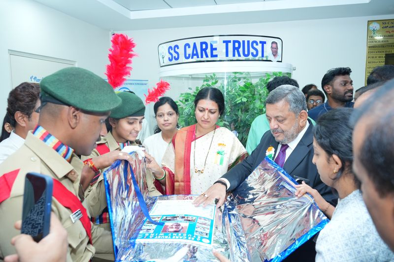 Scouts in uniform and Trust officials unwrap a framed certificate beneath an SS Care Trust sign indoors.