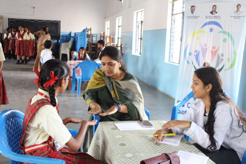 A health worker examines a schoolgirl's hands while a colleague takes notes during a children's health screening session.