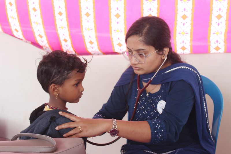 A health worker uses a stethoscope to listen to a young child's chest during a medical check-up.