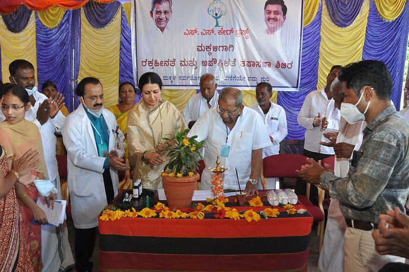 Dignitaries light a ceremonial lamp beside a potted plant at the inaugural function of a children's health camp.