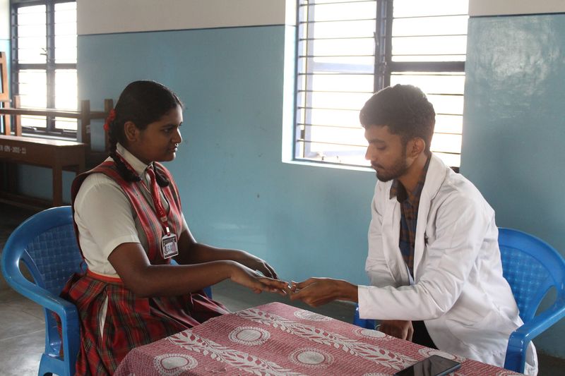 A health worker and a schoolgirl exchange something across a table during a one-on-one health consultation.