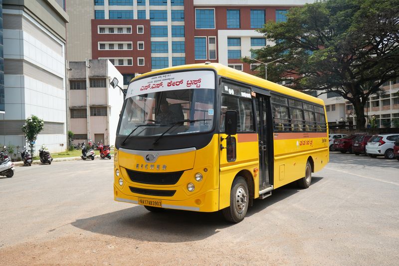 The yellow SS Care Trust bus, with the Trust's name in Kannada above the windscreen, on a college campus.